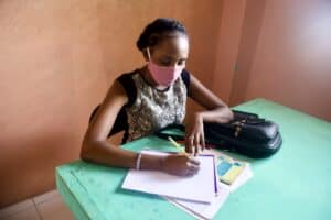 An empowered student with a mask works at an old, wooden, green desk with pencil and paper